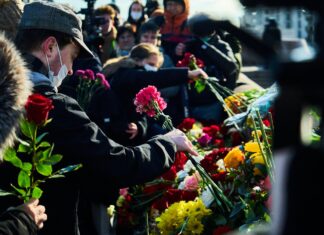 Mourners man in black suit holding bouquet of flowers