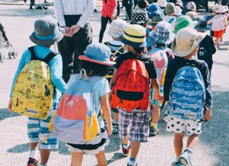 Elementary group of people wearing white and orange backpacks walking on gray concrete pavement during daytime