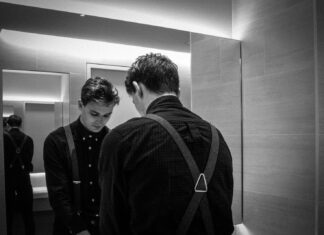 Reflections grayscale photography of man standing front of mirror