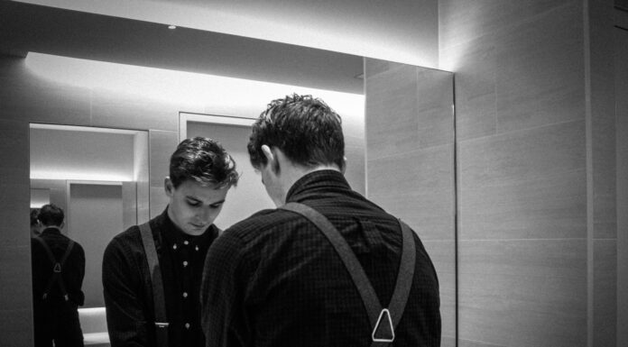 Reflections grayscale photography of man standing front of mirror