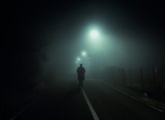 Afterlight man walking at blacktop road with turned on streetlights