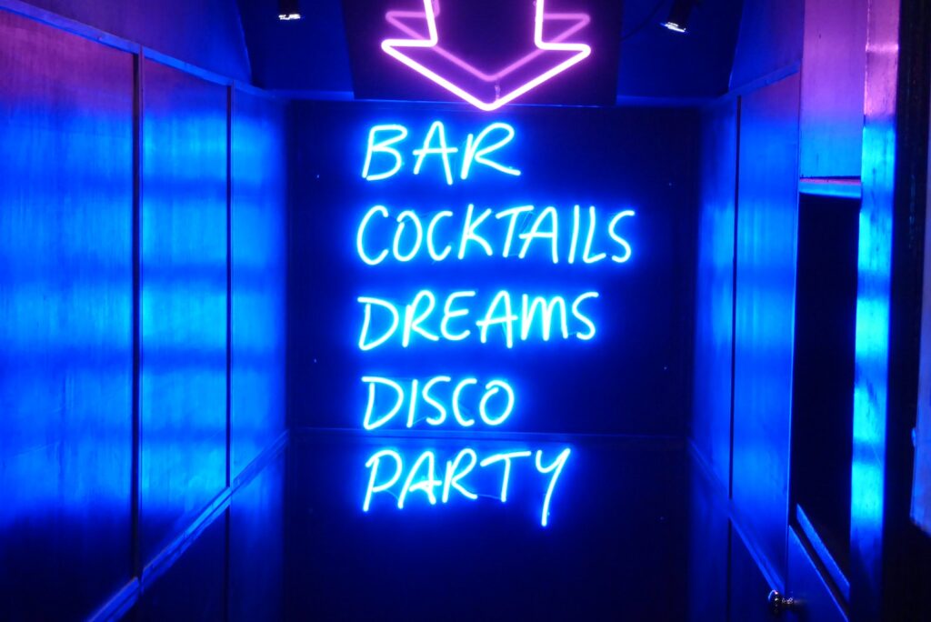 WITH THE NEON LIGHTS OF THE STRIP CLUB FLASHING