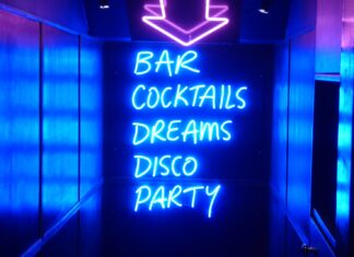 WITH THE NEON LIGHTS OF THE STRIP CLUB FLASHING neon sign reading bar cocktails dreams disco party