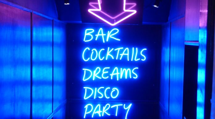 WITH THE NEON LIGHTS OF THE STRIP CLUB FLASHING neon sign reading bar cocktails dreams disco party