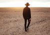 “I Once Was Lost…” man walking on dried plain while looking towards the sun on horizon