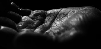 When the Wind Whistles Close-up of a wrinkled hand against black background