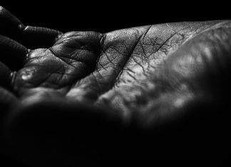 When the Wind Whistles Close-up of a wrinkled hand against black background