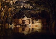 Nyctophilia Stalactites and stalagmites in a dark cave with water.