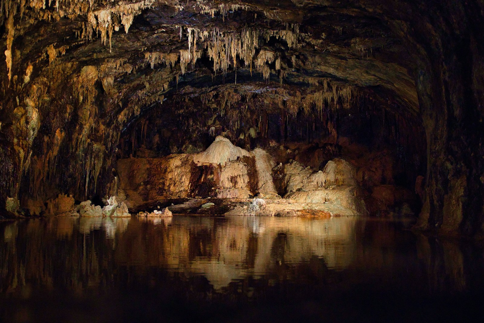 Stalactites and stalagmites in a dark cave with water.