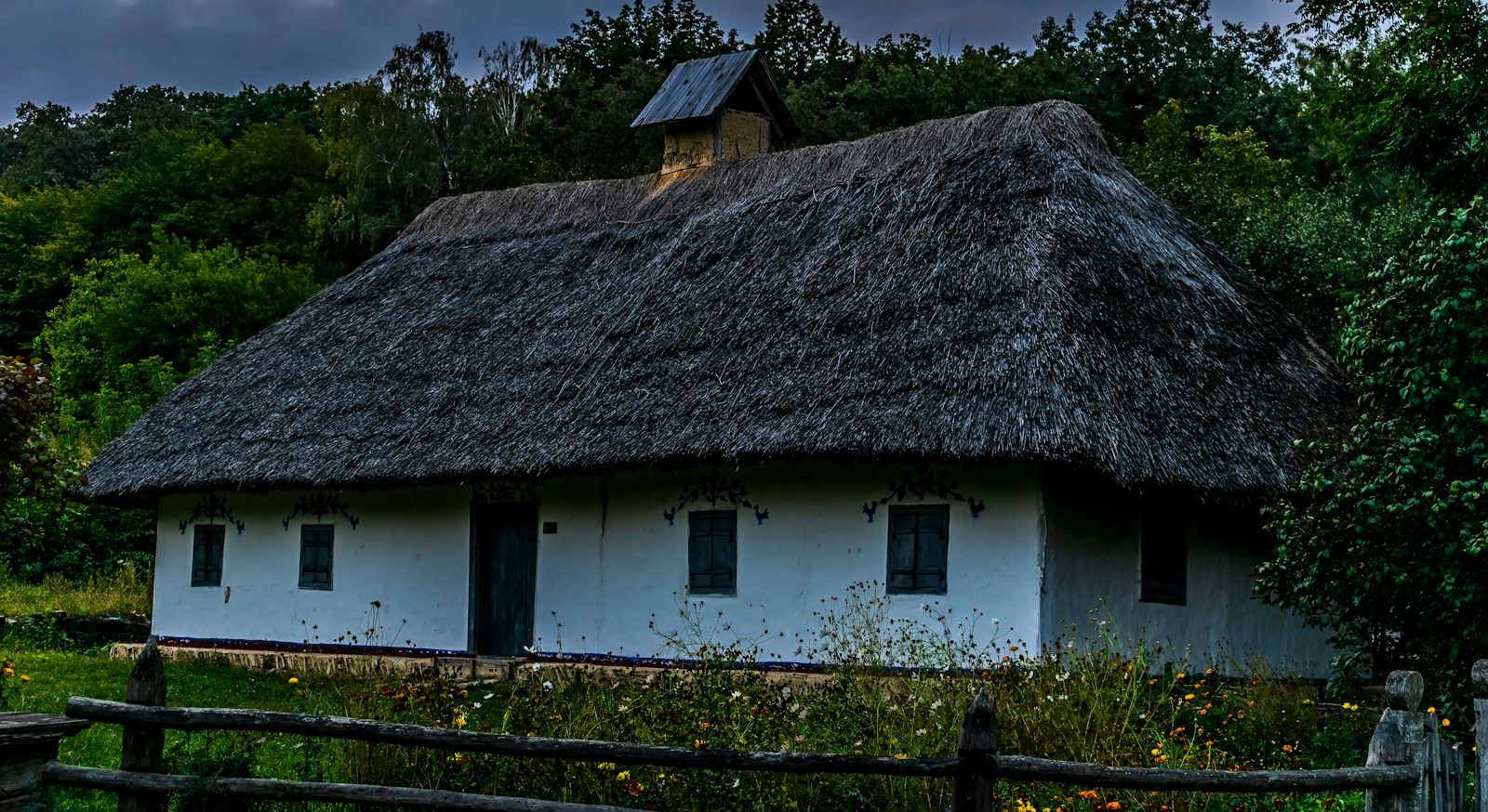 a white house with a thatched roof and a wooden fence